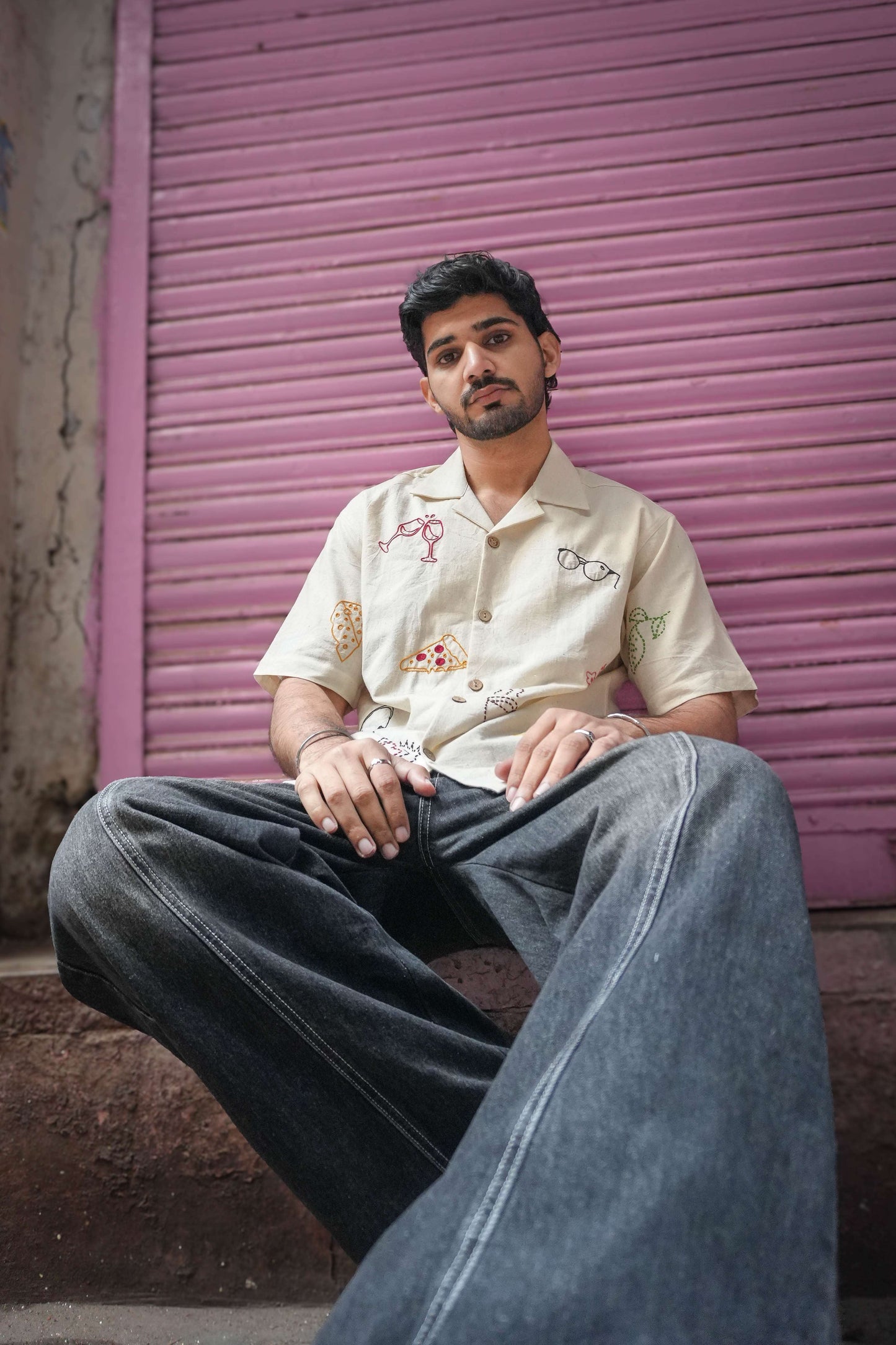 Ivory handloom cotton shirt for men with hand embroidered vacation motifs, seated view