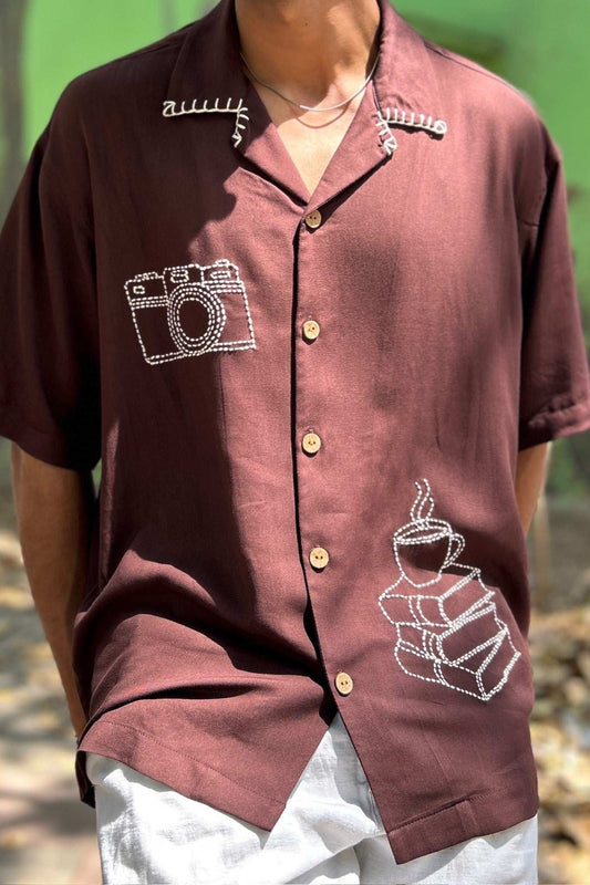 Close-up of camera motif on the right chest and coffee cup on a stack of books at the left waist, brown modal men's shirt