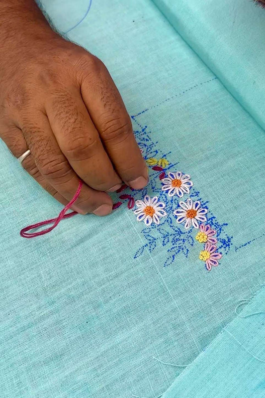 Artisan hand embroidering floral daisy motifs on aqua blue handloom cotton, the making of the Jaipur Embroidered Shirt